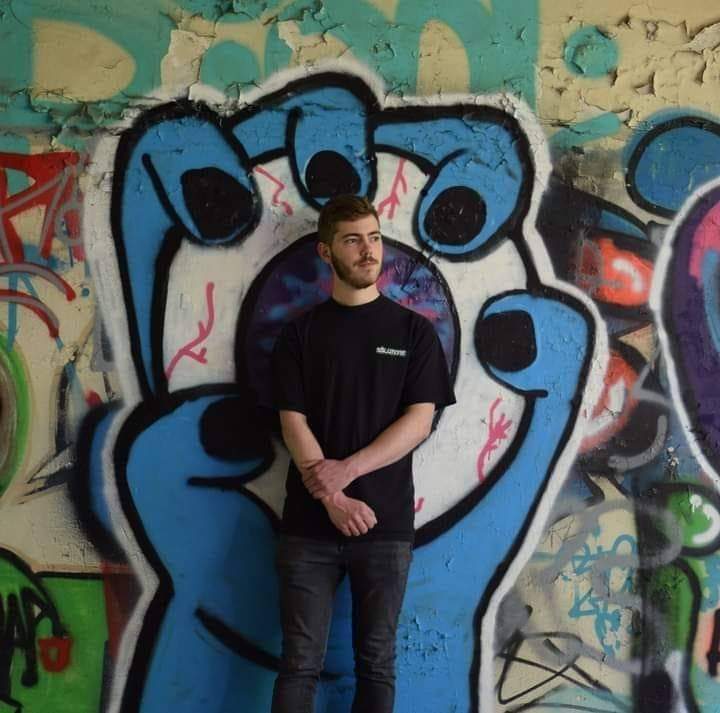 KOLASIN posant devant un mur de graffitis